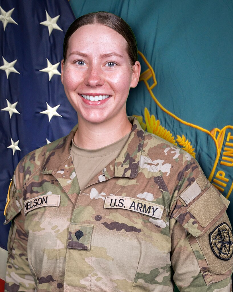 Woman in U.S. Army uniform standing in front of two flags.