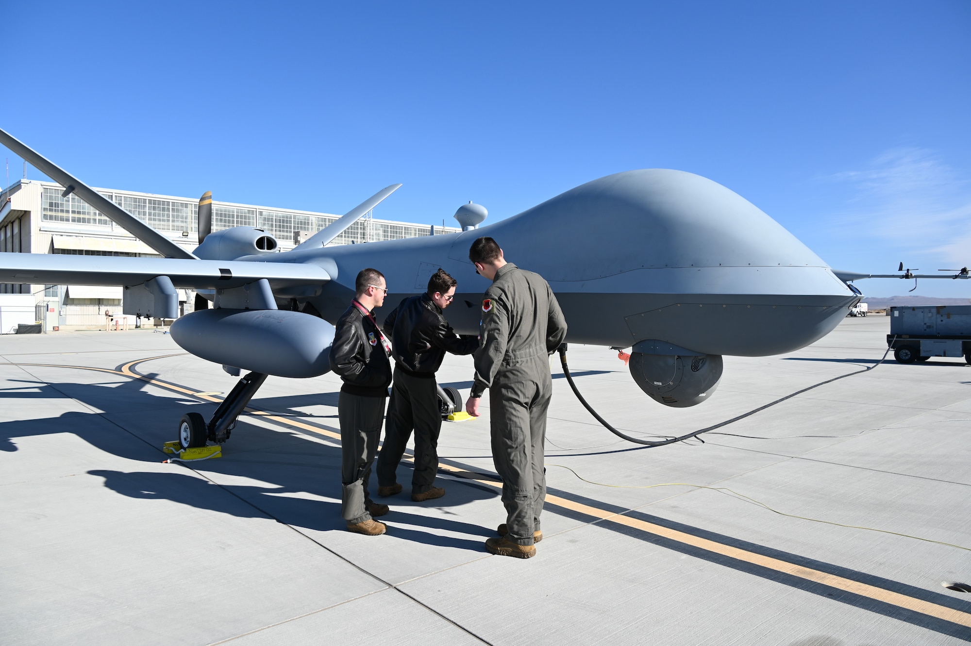 Three men in military uniforms look at an MQ-9 Reaper remotely piloted aircraft.