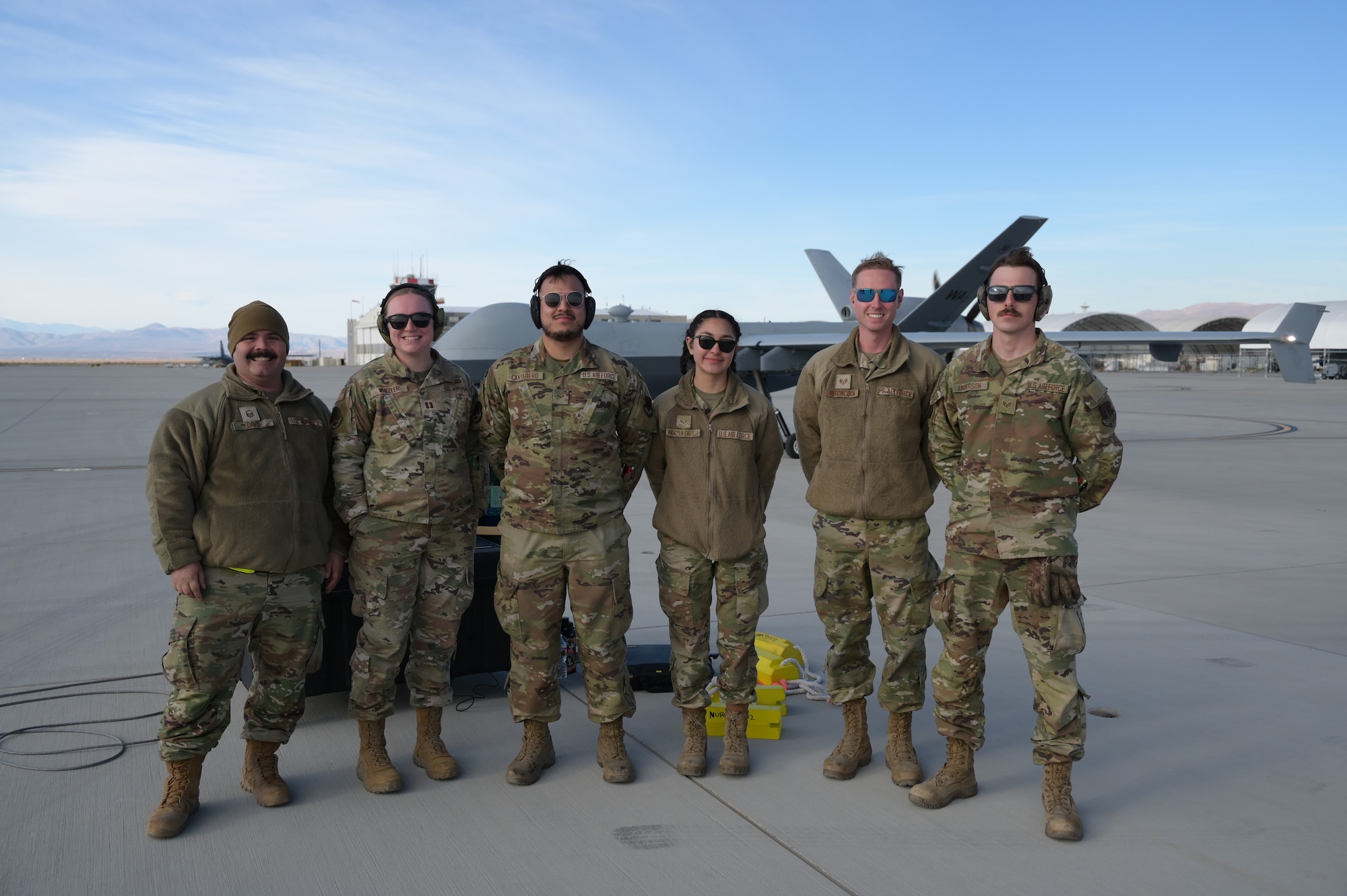 Six people in military uniforms pose for a photo in front of an MQ-9.