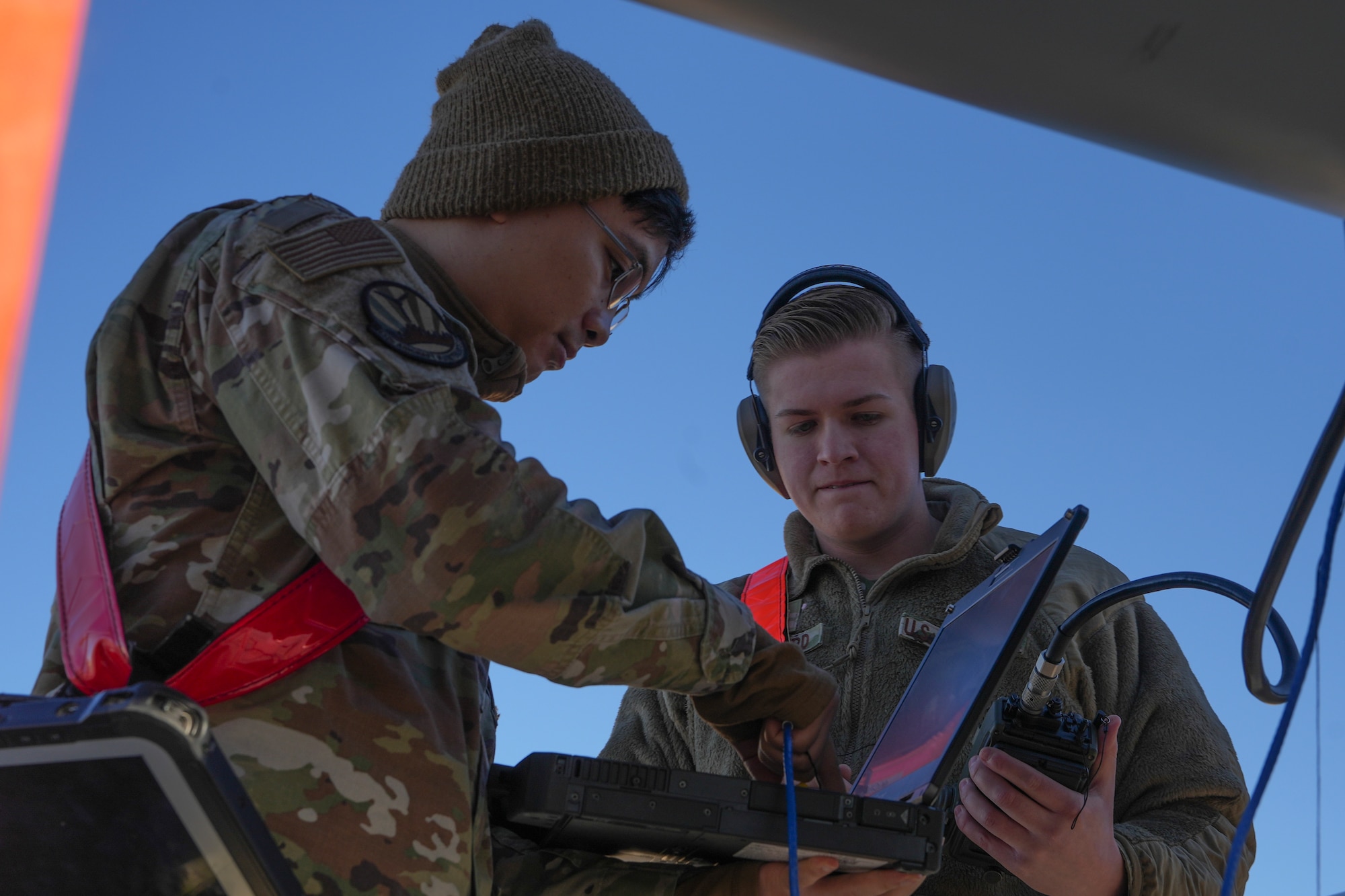 Two men in military uniforms analyze data on a computer.
