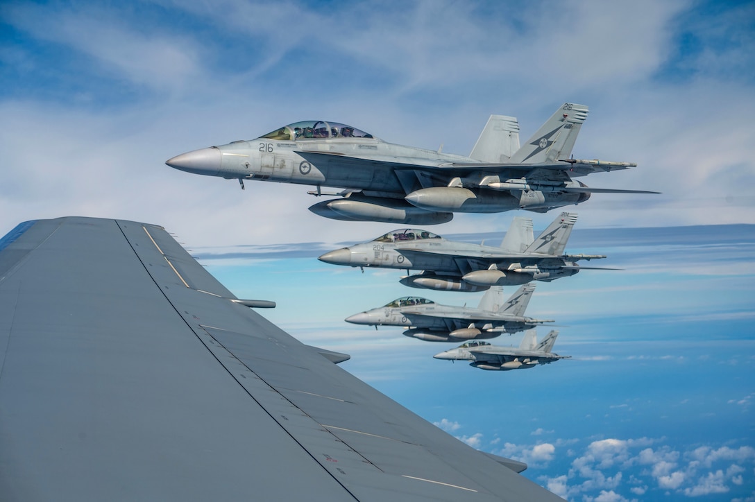Four fighter jets fly in a partly cloudy sky.