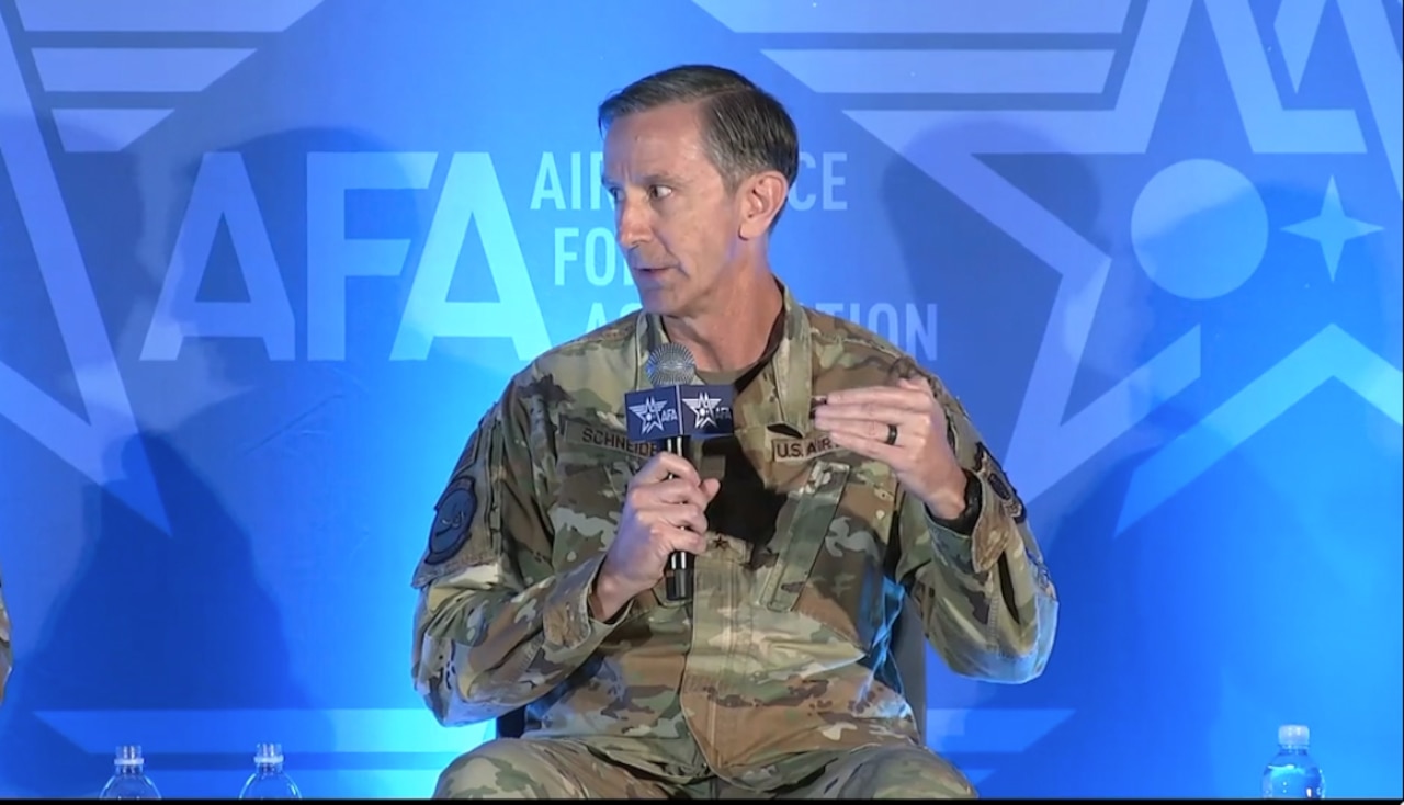 A man wearing a military uniform with a microphone in his hand speaks to the crowd.