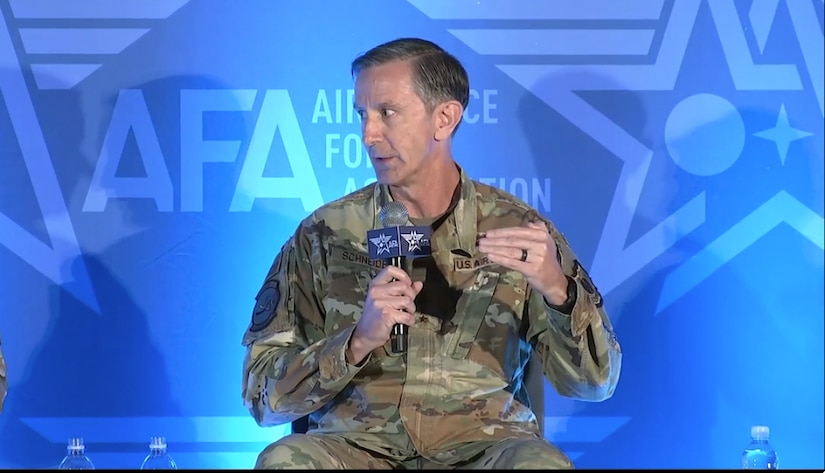 A man wearing a military uniform with a microphone in his hand speaks to the crowd.