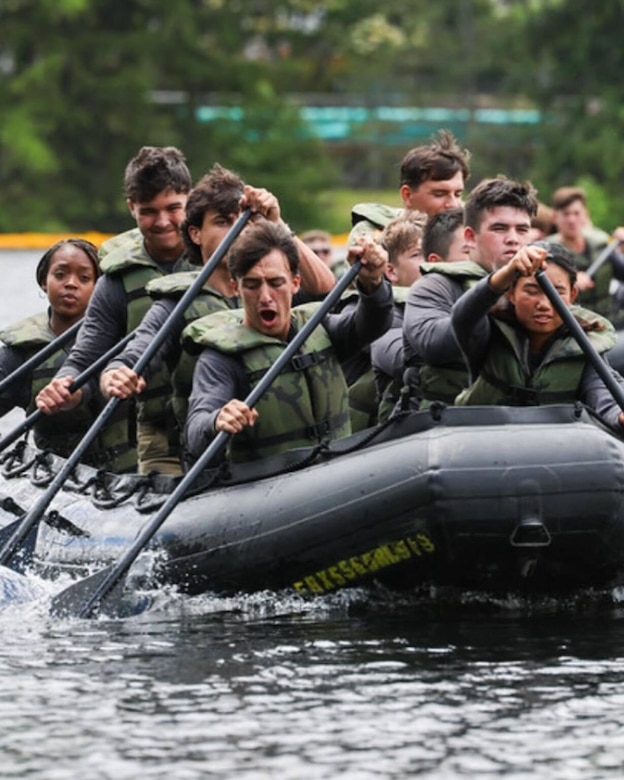 Men and women wearing life preservers rowing on an inflatable boat.