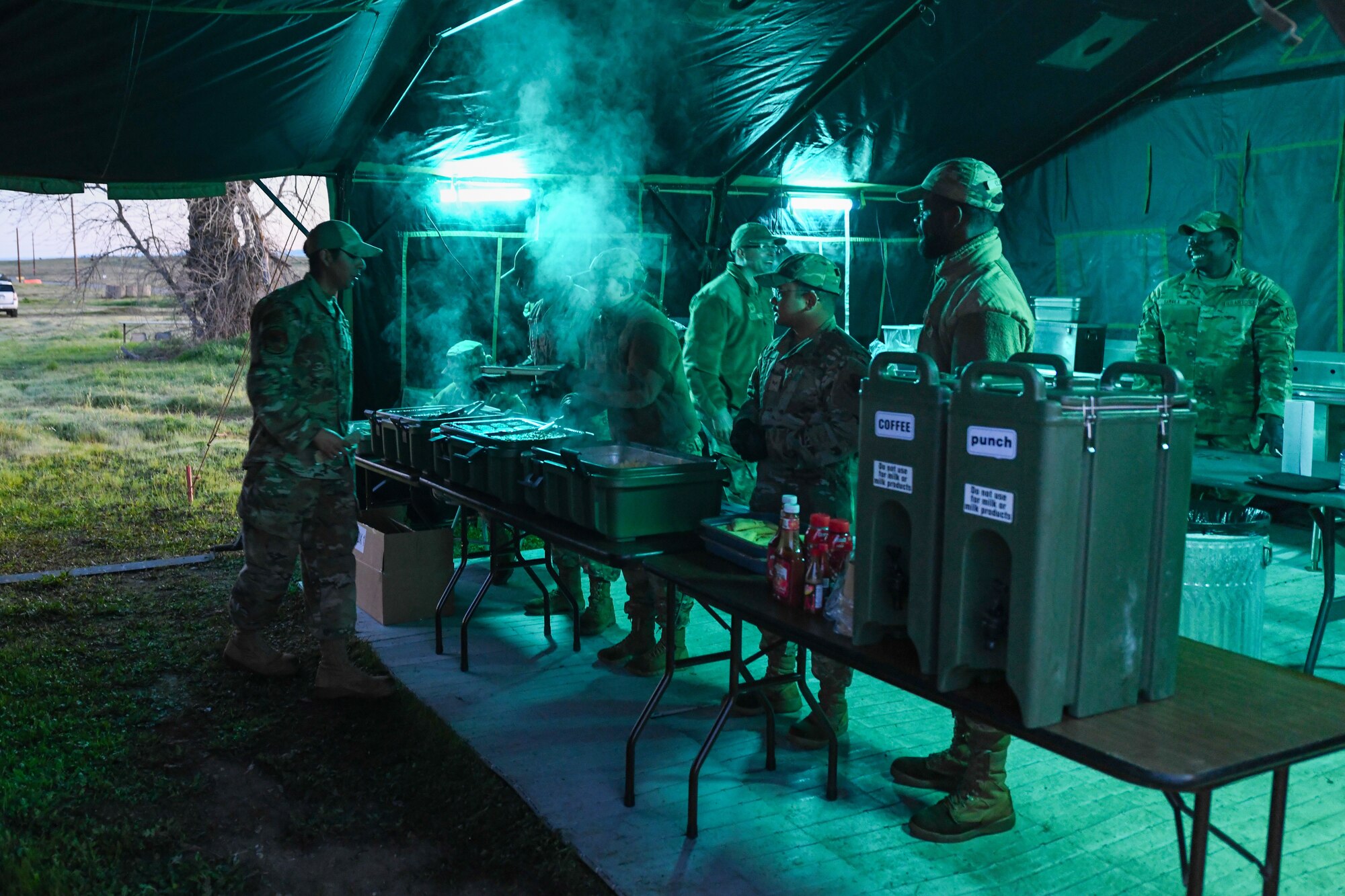 Airmen gather together under a tent for dinner