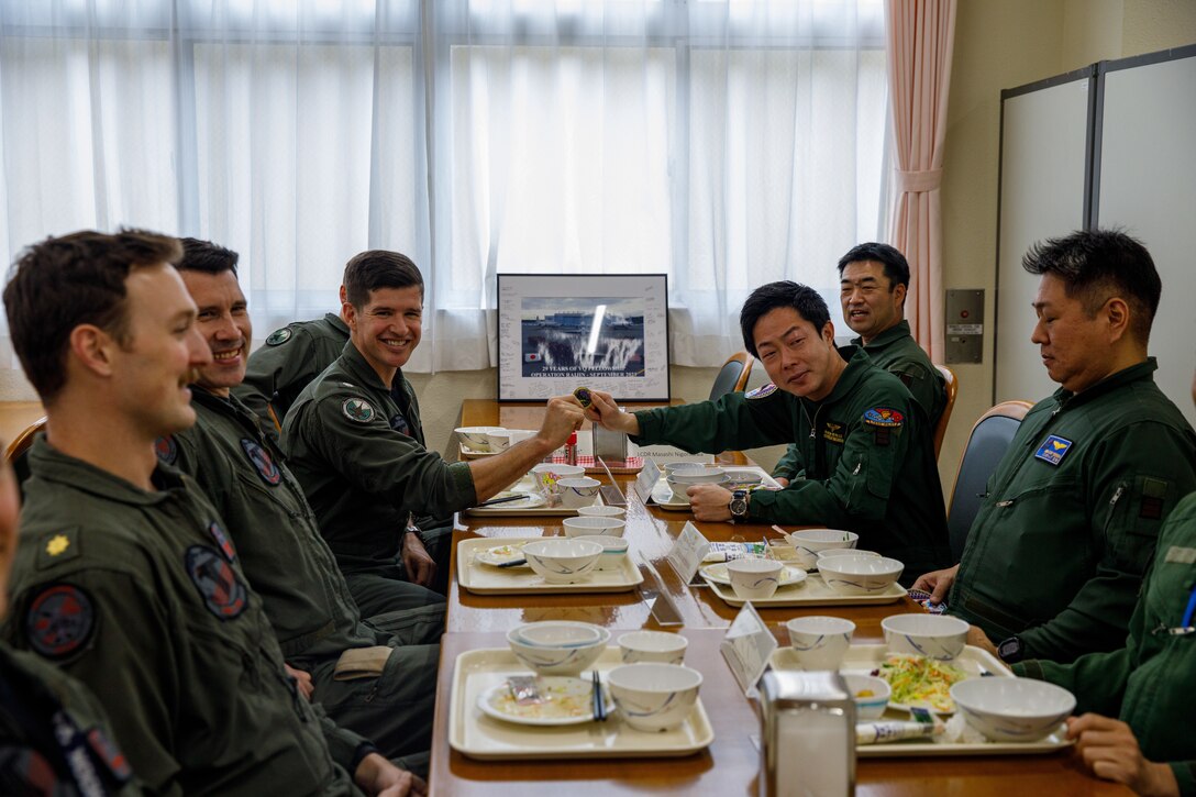 A Japan Maritime Self-Defense Force member with Air Electronic Warfare Squadron (VQ) 81, gives a challenge coin to U.S. Navy Cmdr. Reid Smith, the commanding officer of Electronic Attack Squadron (VAQ) 141, Carrier Air Wing 5, and a native of Washington, during a leadership lunch at Marine Corps Air Station Iwakuni, Japan, March 3, 2025. Leadership from VAQ-141 and VQ-81 met to discuss future training, share information, and strengthen cooperation between the two units. (U.S. Marine Corps photo by Lance Cpl. David Getz)