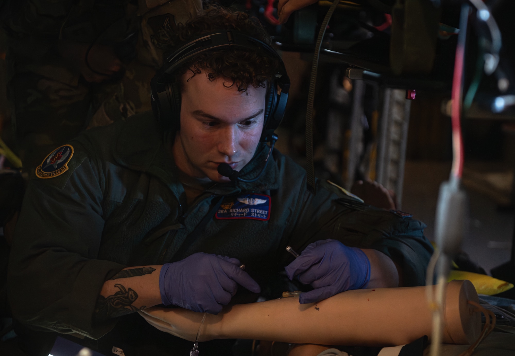 A man holding an intravenous tube prepares to insert it into the arm of a training dummy.