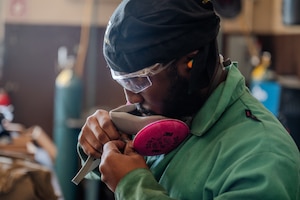 An Airman puts on a mask to ventilate debri from injuring his lungs while sanding a piece of metal.