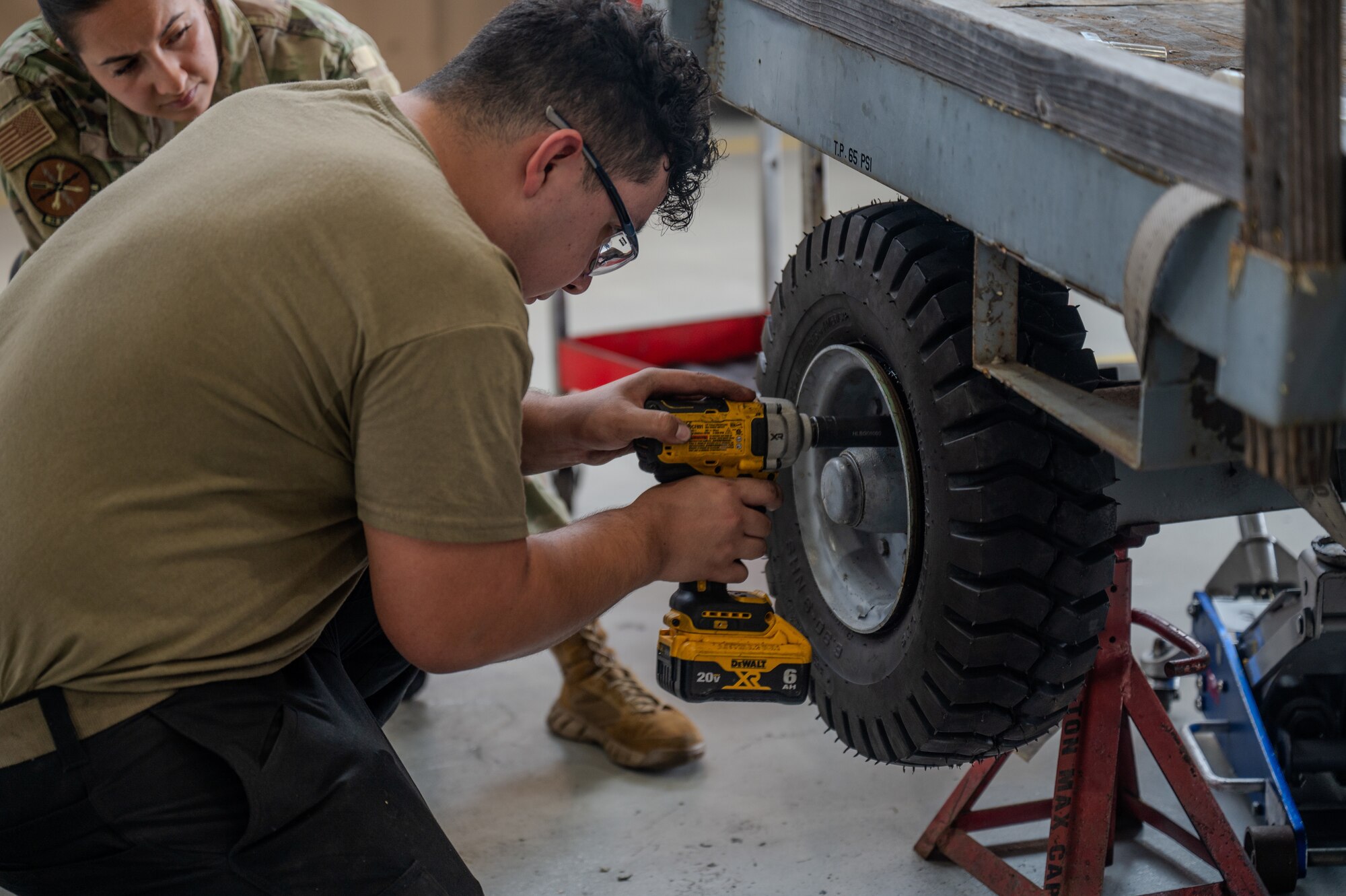 An Airman is kneeling down while using a tool to unscrew a bolt that is holding a tire.