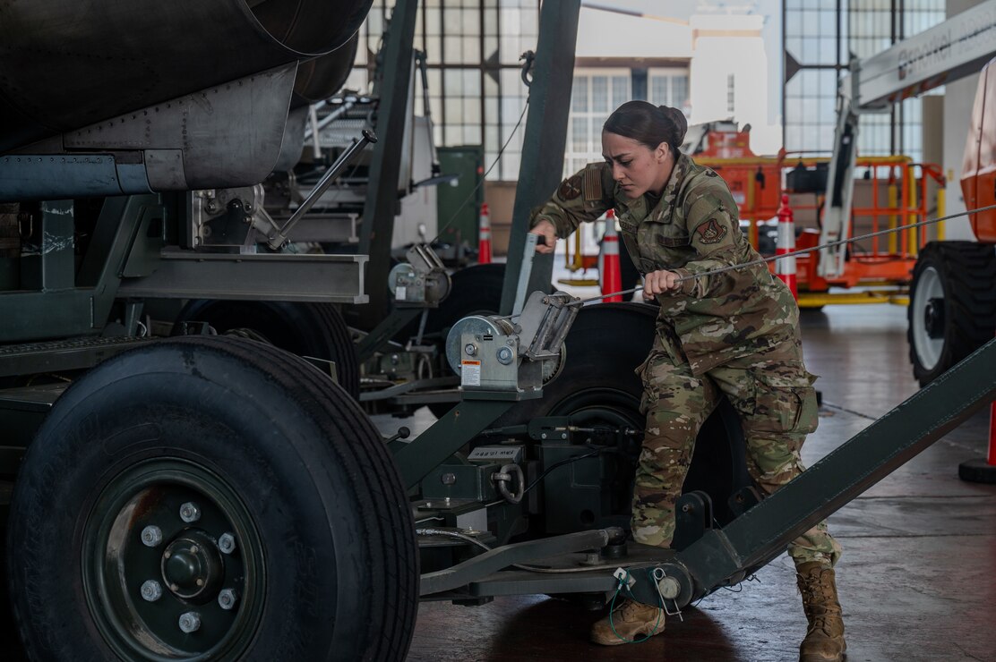 An Airman pumps a lever up and down on a trailer holding an Aircraft engine.