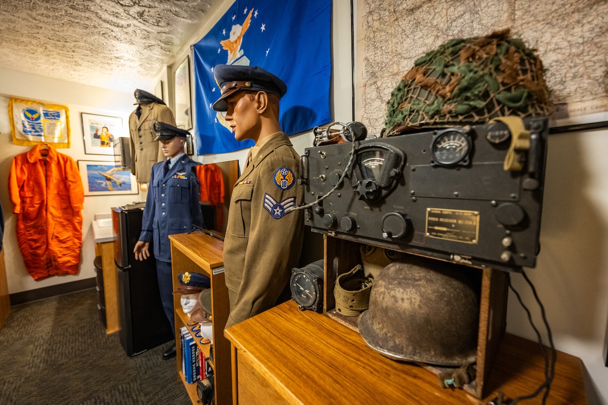 Vintage military uniforms and memorabilia on display, a large military HAM radio with two helmets sits prominently in the foreground