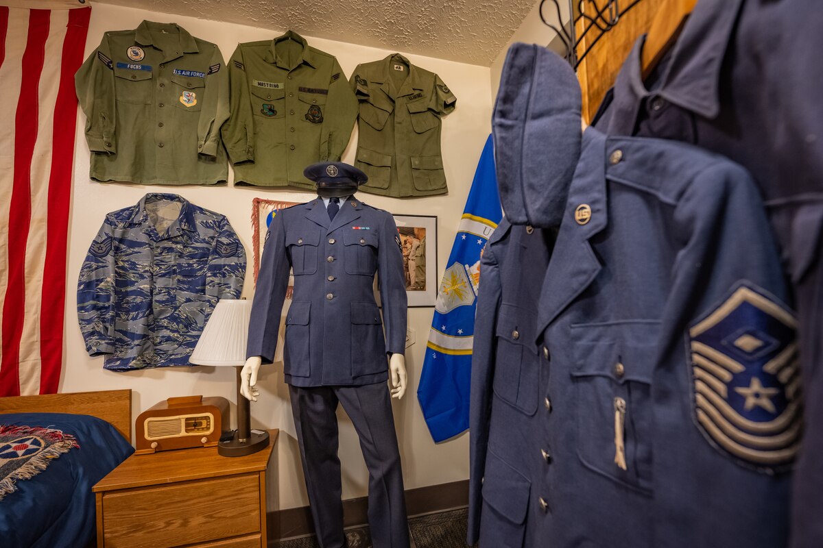 Vintage military uniforms and memorabilia on display, a First Sgt. diamond sewed onto a service jacket hangs prominently in the foreground