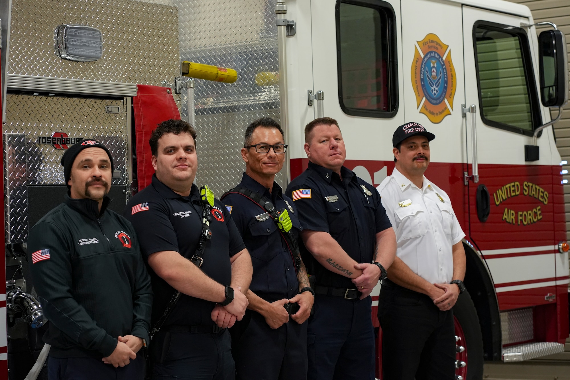 A group of firefighters pose in front a fire truck.