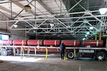 People in a large warehouse stand next to a flatbed truck that is loaded with red canisters.