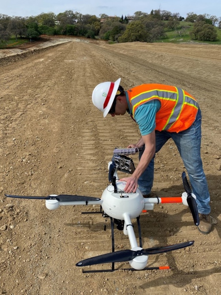 A man with a hard hat and protective vest looks over a Quad-Copter Unmanned aerial system.