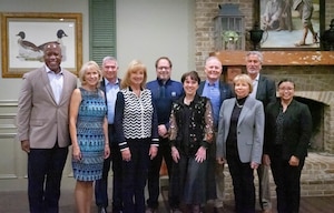 Five men and 5 women stand in front of a fireplace, smiling at the camera.