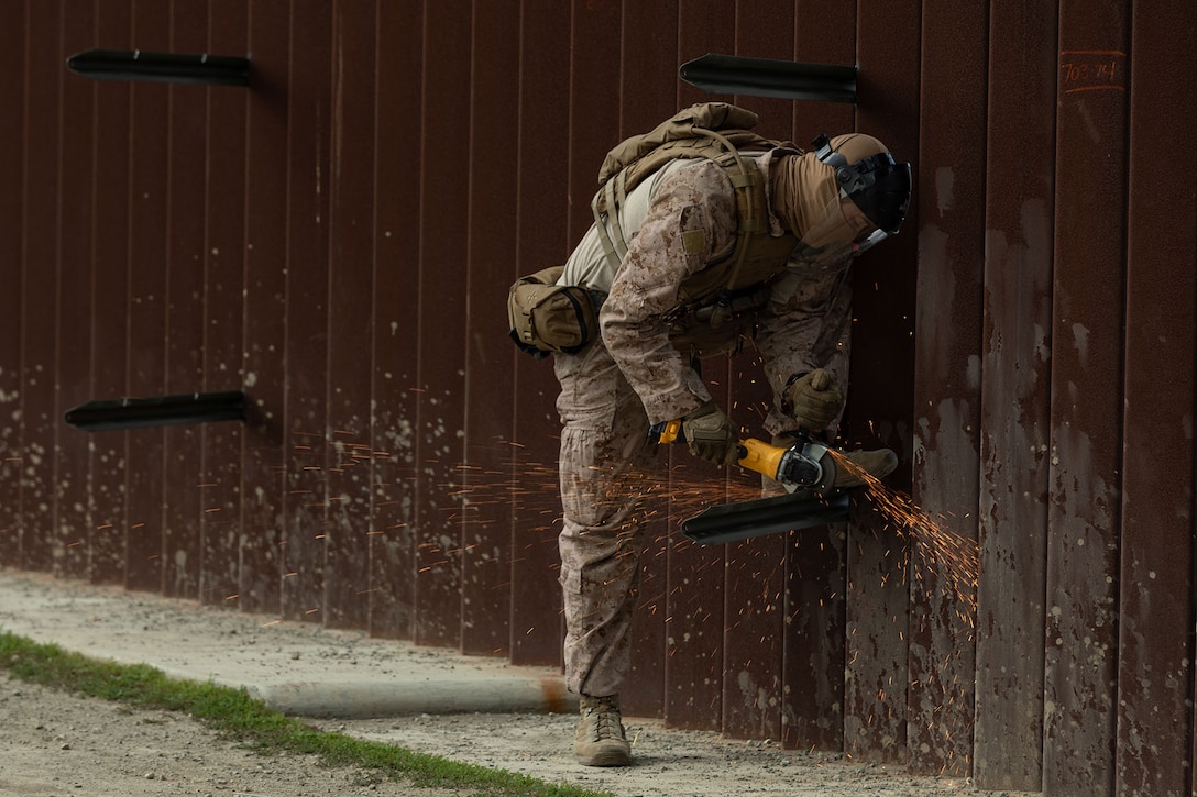 Sparks fly as a Marine welds medal near a fence.