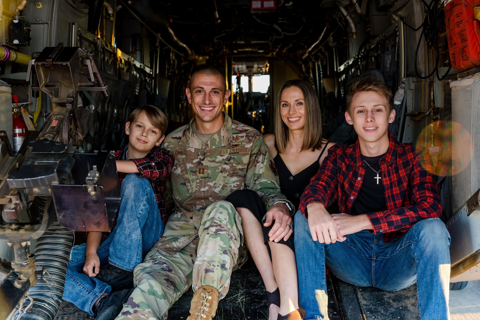 Two white male teens in red buffalo plaid, white male in Air Force uniform and white woman in black dress all sit together inside helicopter.