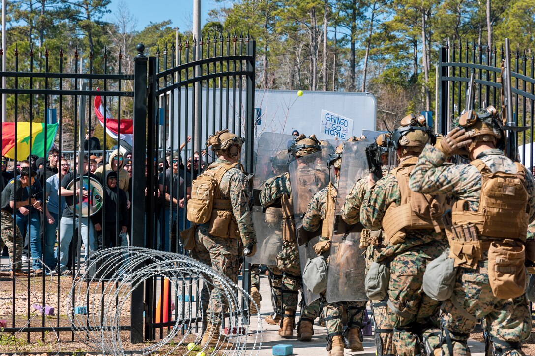 U.S. Marines and Sailors with Golf Company, 2nd Battalion, 2nd Marine Regiment prepare to protect a simulated embassy compound against a riot during an embassy reinforcement training mission at Marine Corps Base Camp Lejeune, North Carolina, Feb. 23, 2024. As the command element of a Marine Air-Ground Task Force, the 26th Marine Expeditionary Unit completed a certification exercise, conducted by Expeditionary Operations Training Group, to prepare for a diverse range of potential future missions, including personnel recovery, embassy reinforcement, foreign humanitarian assistance, and non-combatant evacuation operations. (U.S. Marine Corps photo by Lance Cpl. Jack Labrador)