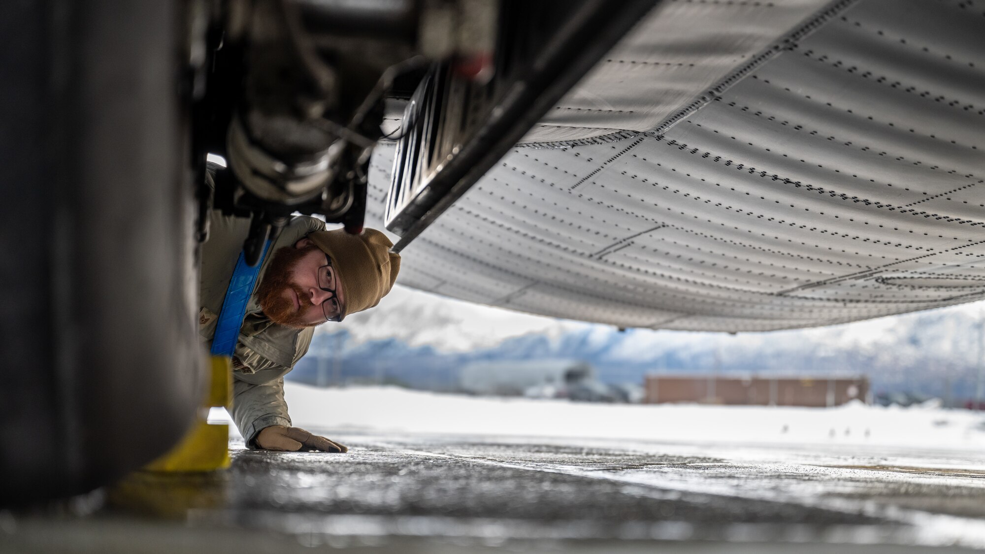U.S. Air Force Tech. Sgt. Tyler Nelson, 317th Aircraft Maintenance Squadron flying crew chief and Lethal Expeditionary Airman Development course graduate, checks under a C-130J Super Hercules during Joint Pacific Multinational Readiness Center exercise 25-02 at Joint Base Elmendorf-Richardson, Alaska, Jan. 22, 2025. Nelson’s maintenance team performed routine safety inspections to identify challenges in extreme cold weather conditions to ensure the 40th Airlift Squadron could deliver fully mission-capable aircraft and integrate with nearly 10,000 Department of Defense service members during JPMRC 25-02. (U.S. Air Force photo by Airman 1st Class Jade M. Caldwell)