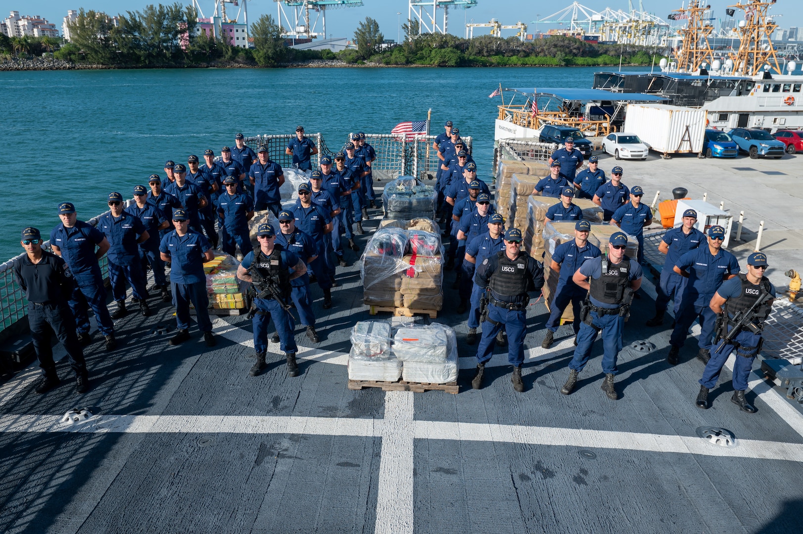 Crew members from USCGC Valiant (WMEC 621) stand at parade rest in front of interdicted narcotics at Base Miami Beach, Florida, Mar. 6, 2025. The Valiant's crew secured the illegal drugs from six interdictions in the international waters of the Caribbean. (U.S. Coast Guard photo by Petty Officer 3rd Class Nicholas Strasburg)