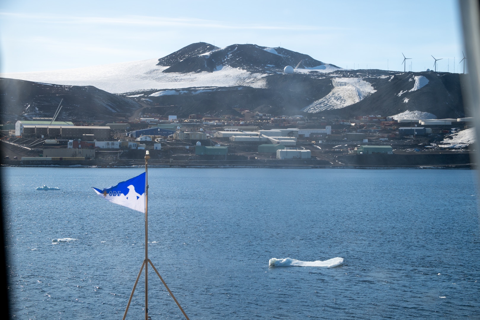 The U.S. Antarctic Program’s NSF McMurdo Station sits in the distance while U.S. Coast Guard Cutter Polar Star (WAGB 10) prepares to moor in Winter Quarters Bay during Operation Deep Freeze, Feb. 13, 2025.  U.S. Indo-Pacific Command continues to lead the Joint Task Force-Support Forces Antarctica team in providing logistic support for the United States Antarctic Program. (U.S. Coast Guard photo by Petty Officer 2nd Class Briana Carter)