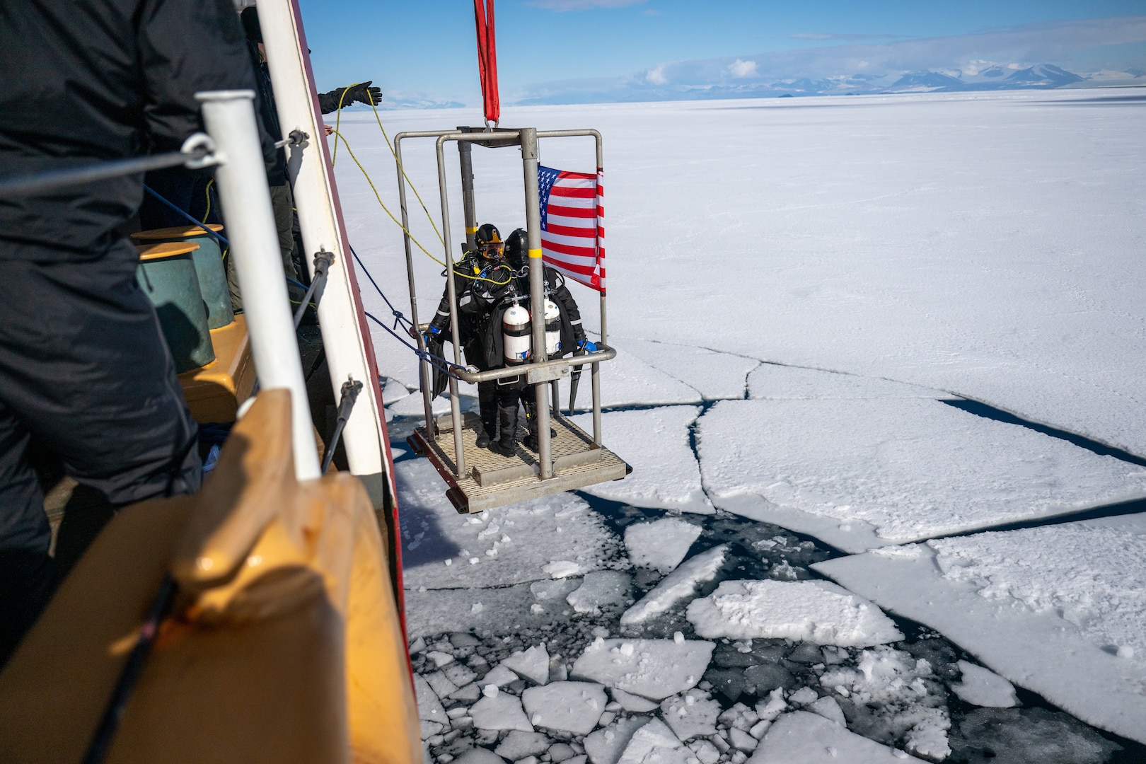 Petty Officer 2nd Class Forrest Parker and Petty Officer 2nd Class Richard Rudek, Coast Guard divers from Regional Dive Locker Pacific, are lowered into  McMurdo Sound by U.S. Coast Guard Cutter Polar Star (WAGB 10) during Operation Deep Freeze, Jan. 13, 2025. Every year, a joint and total force team works together to complete Operation Deep Freeze. Active, Guard, and Reserve service members from the U.S. Air Force, Army, Coast Guard, and Navy work together to forge a strong Joint Task Force-Support Forces Antarctica (JTF-SFA) that continues the proud tradition of U.S. military support to the United States Antarctic Program. (U.S. Coast Guard photo by Petty Officer 2nd Class Briana Carter)