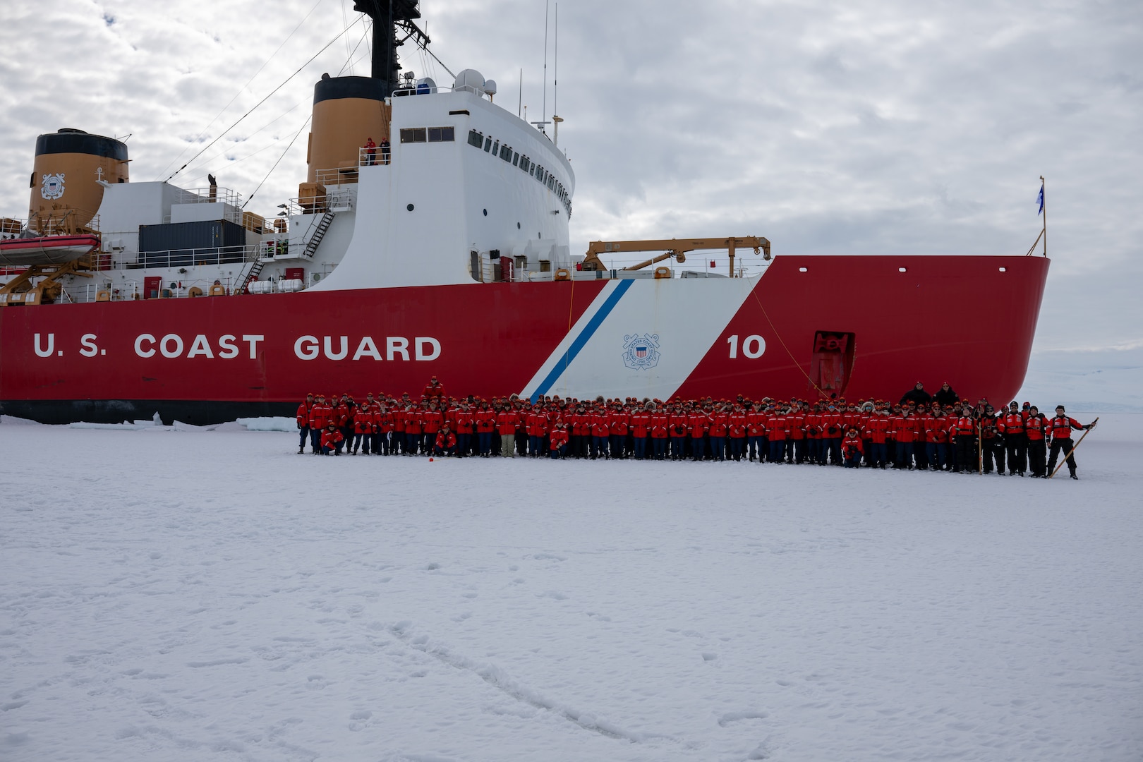 The crew of U.S. Coast Guard Cutter Polar Star (WAGB 10) stand for a photo while the cutter is hove-to in McMurdo Sound during Operation Deep Freeze, Jan. 7, 2025. Polar Star is conducting ice-breaking operations in Antarctica in support of Operation Deep Freeze, a joint service, inter-agency support operation for the National Science Foundation, which manages the United States Antarctic Program.  (U.S. Coast Guard photo by Petty Officer 2nd Class Briana Carter)