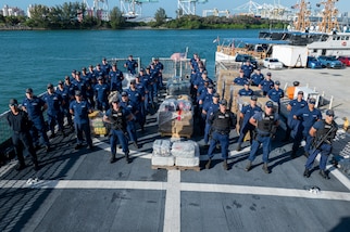 Crew members from USCGC Valiant (WMEC 621) stand at parade rest in front of interdicted narcotics at Base Miami Beach, Florida, Mar. 6, 2025. The Valiant's crew secured the illegal drugs from six interdictions in the international waters of the Caribbean. (U.S. Coast Guard photo by Petty Officer 3rd Class Nicholas Strasburg)