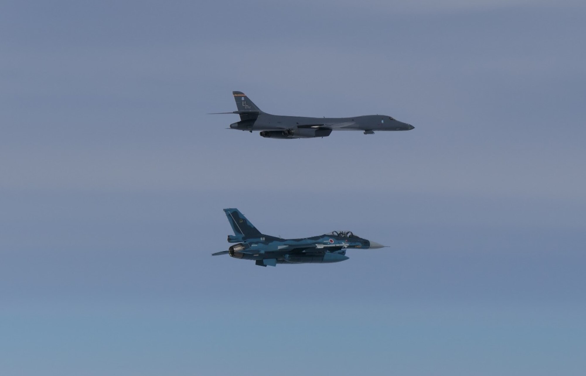 Two military jets, one large and long, and the other short and small, fly close to each other.