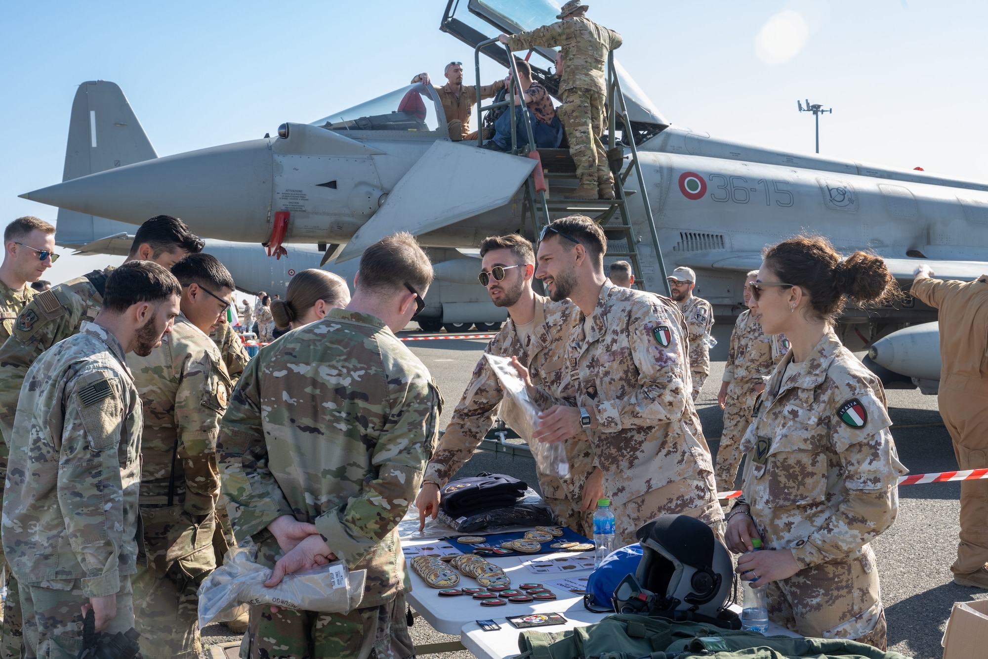 U.S. and Italian service members interact in front of a fighter jet at an air expo.