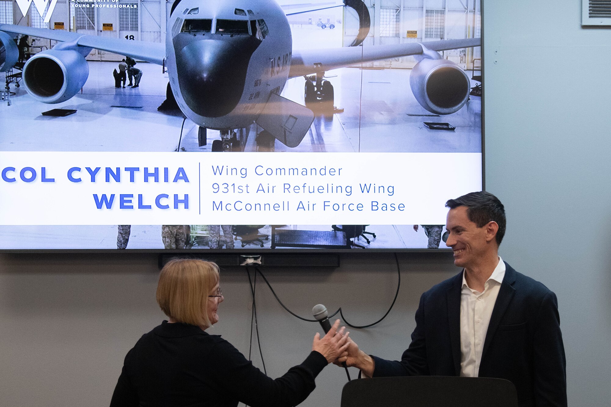 Col. Cory Damon, 22nd Air Refueling Wing commander, hands the microphone to Col. Cynthia Welch, 931st Air Refueling Wing commander, at the Kansas Aviation Museum in Wichita, Kansas, March 4, 2025. Mission Wichita is a program that connects McConnell Airmen and Wichita locals to reinforce the relationship between the military and young professionals within the community. (U.S. Air Force photo by Airman 1st Class Patrick O'Neill)