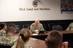 A man in a military uniform sits at the head of a table in a meeting with several others in military uniform.