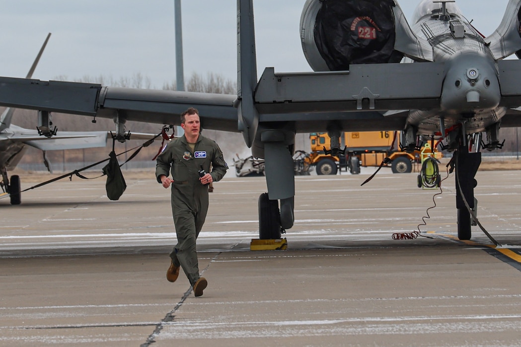 Male pilot in flight suit running in front of an A-10 Thunderbolt II attack jet.