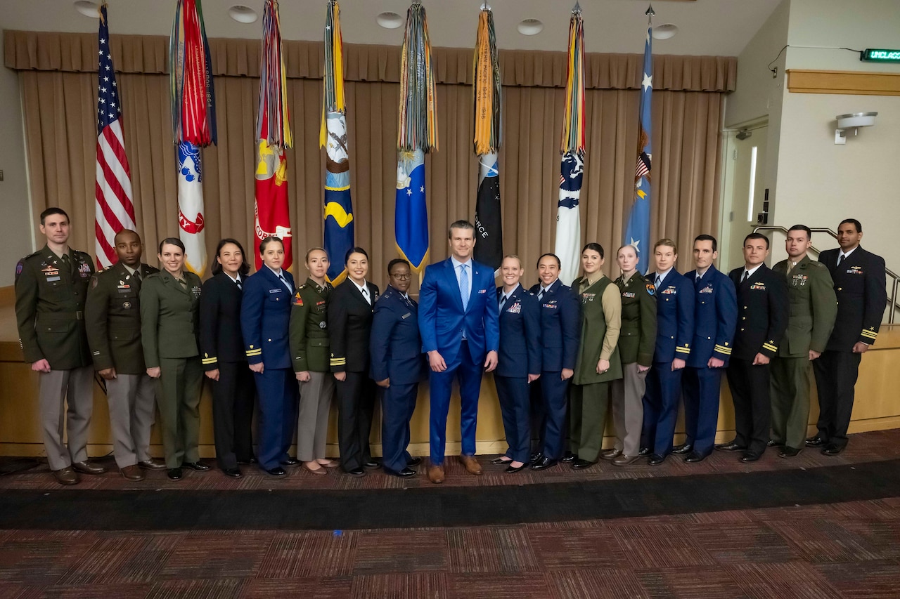 A man in a civilian suit is flanked by more than a dozen military officers.