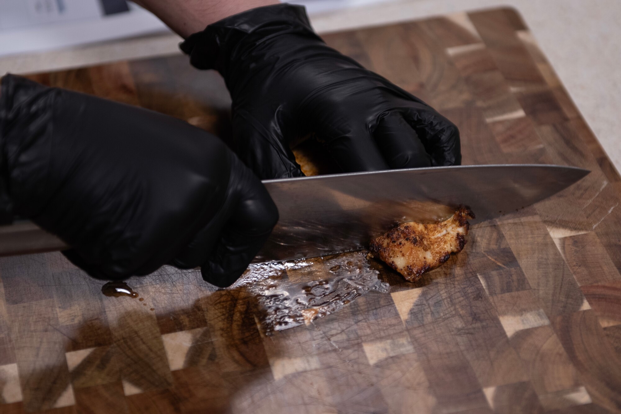 A U.S. Air Force enlisted aide assigned to Air Force Special Operations Command cuts chicken on a cutting board during a Cooking with Command event at Hurlburt Field, Florida, Feb. 11, 2025.