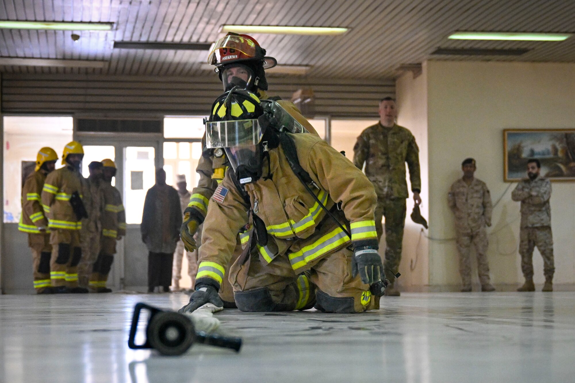 Two firefighters kneel while simulating fire training.