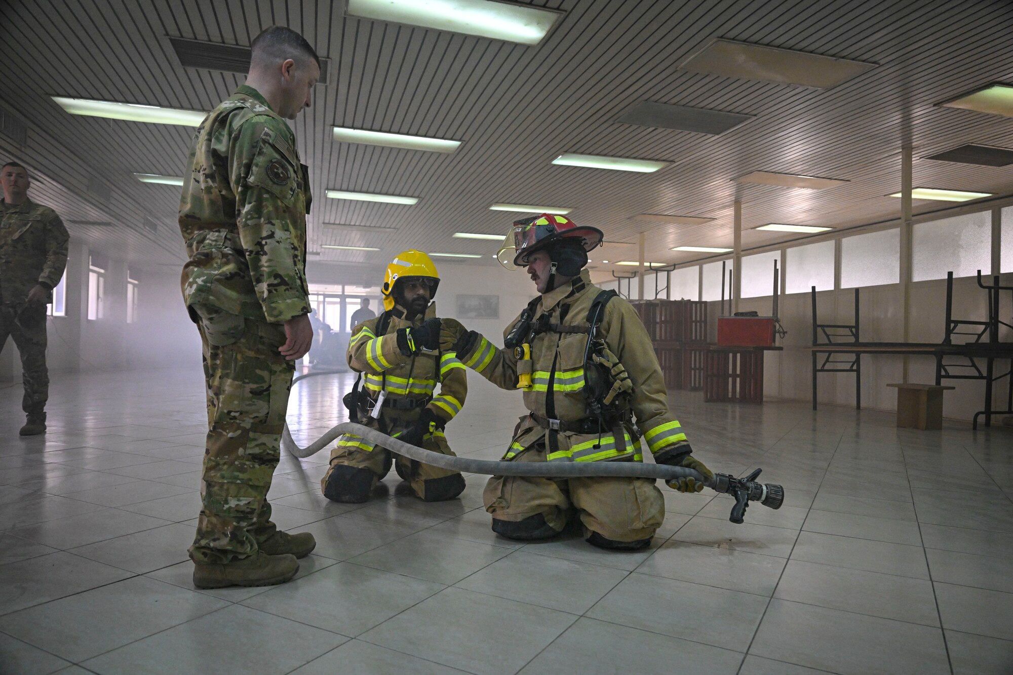 Two firefighters kneel and fist bump as another firefighter stands in front of them.