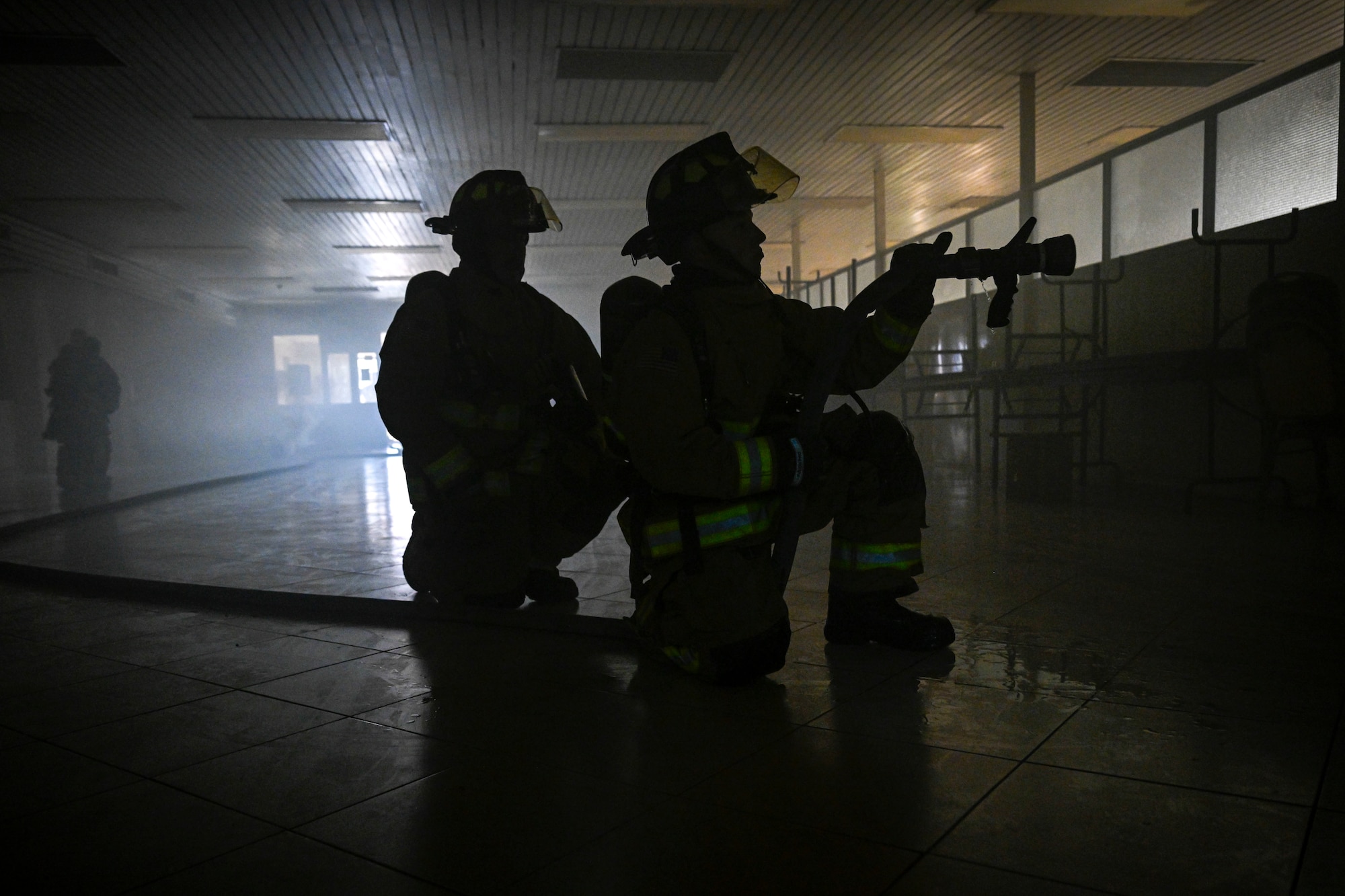 Two firefighters kneel in a dark room.
