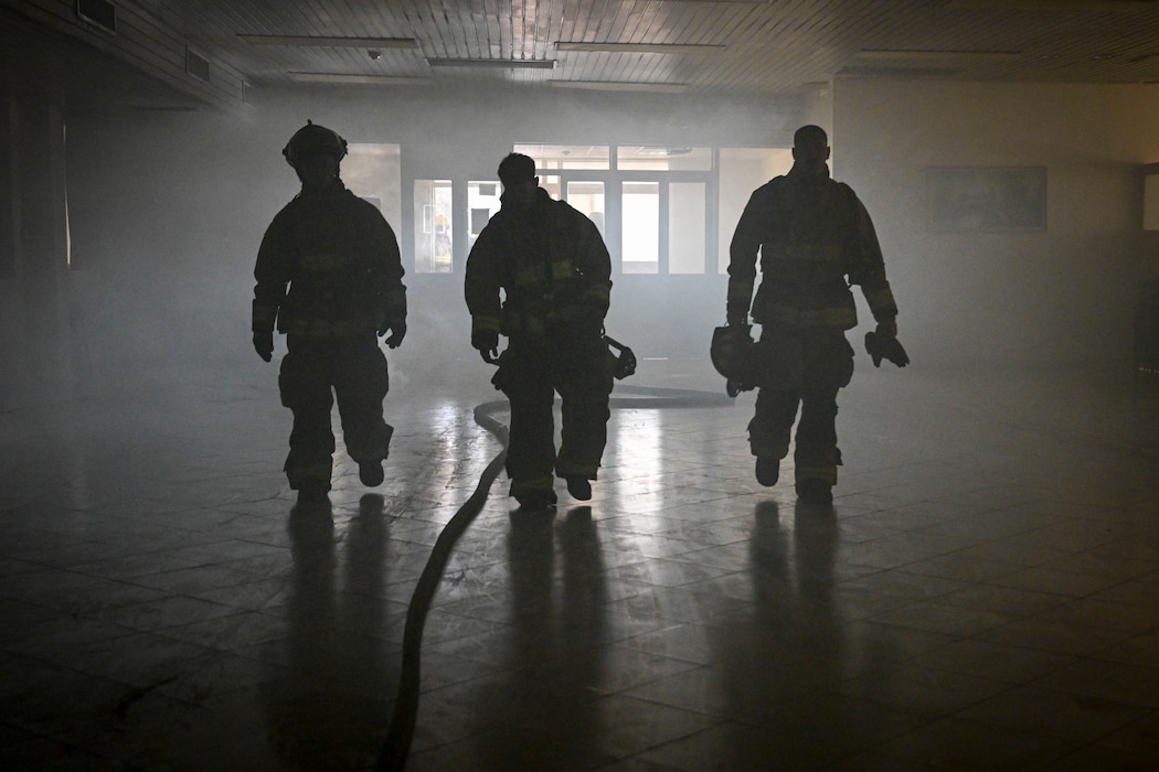 Three firefighters walk in a dark room.