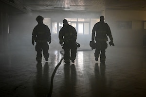 Three firefighters walk in a dark room.