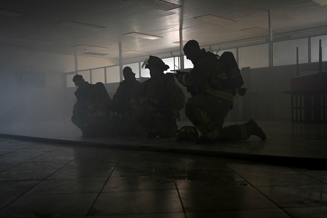 Four firefighters kneel in a dark room.