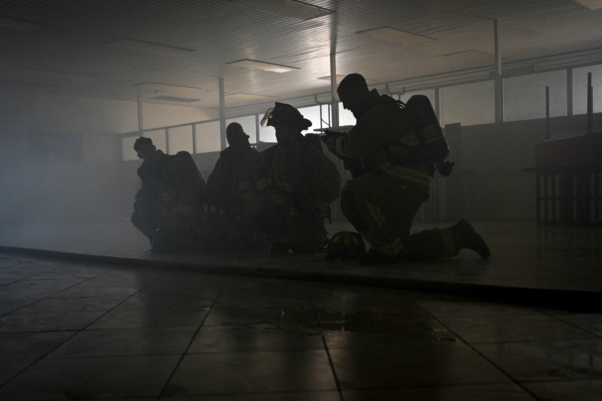 Four firefighters kneel in a dark room.