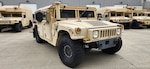 A tan HMMWV parked on concrete with other military vehicles behind.