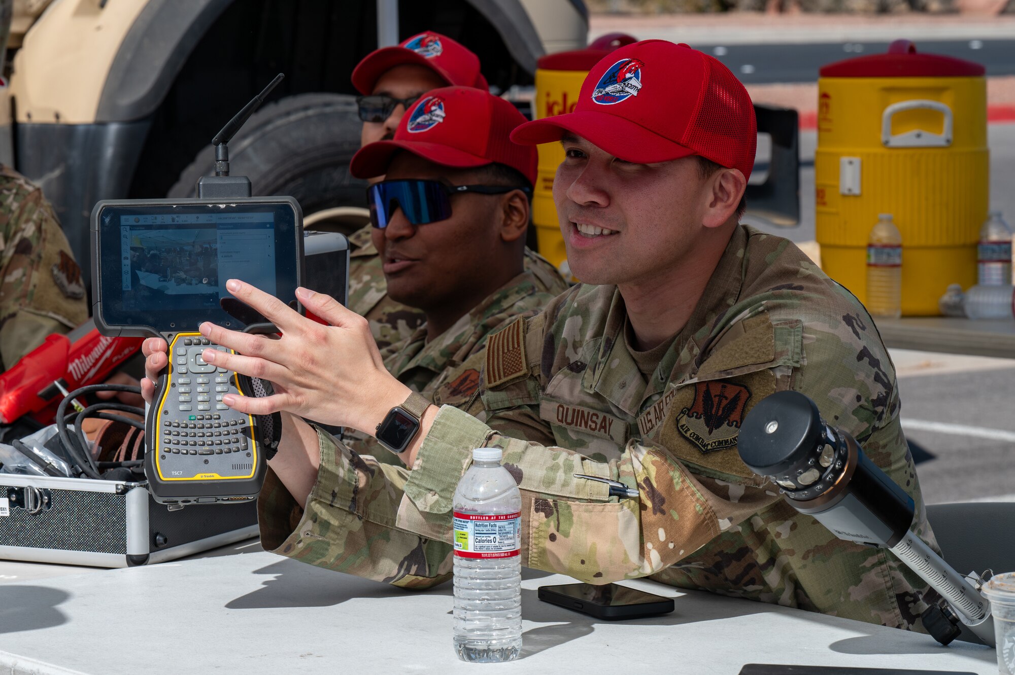 An Airman holds a Trimble receiver while seated at a Construction Career Day booth.