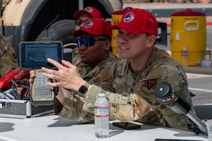 An Airman holds a Trimble receiver while seated at a Construction Career Day booth.