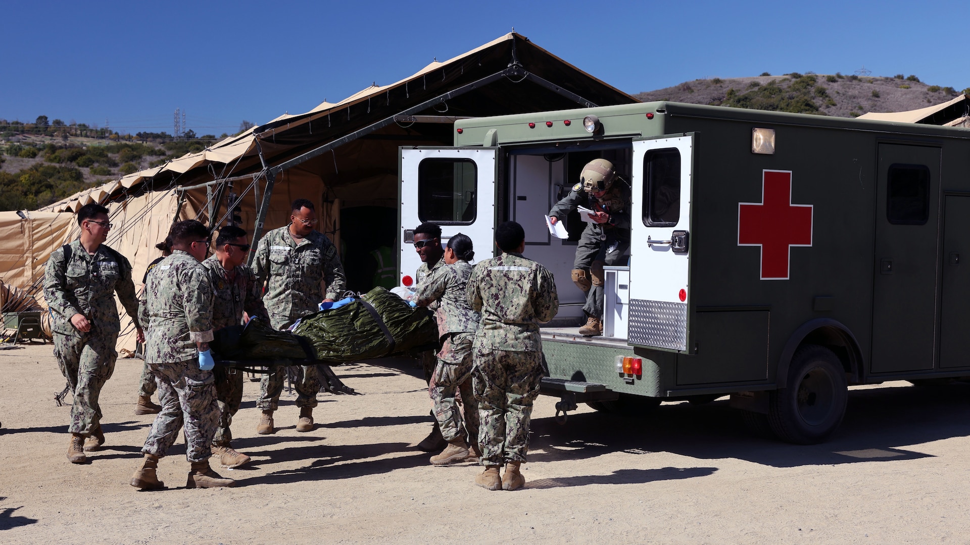 The casualty receiving team of Expeditionary Medical Facility (EMF) 150-Alpha unloads a simulated patient from an ambulance in front of the facility during an EMF training and Operational Readiness Evaluation (ORE) at the Naval Expeditionary Medicine Warfighter Development Center (NEMWDC), Camp Pendleton, Calif., Feb. 15-28. An EMF is a role 3 platform, designed to provide in-theater hospitalization with a hold capacity of up to 150 beds.