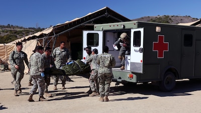 The casualty receiving team of Expeditionary Medical Facility (EMF) 150-Alpha unloads a simulated patient from an ambulance in front of the facility during an EMF training and Operational Readiness Evaluation (ORE) at the Naval Expeditionary Medicine Warfighter Development Center (NEMWDC), Camp Pendleton, Calif., Feb. 15-28. An EMF is a role 3 platform, designed to provide in-theater hospitalization with a hold capacity of up to 150 beds.
