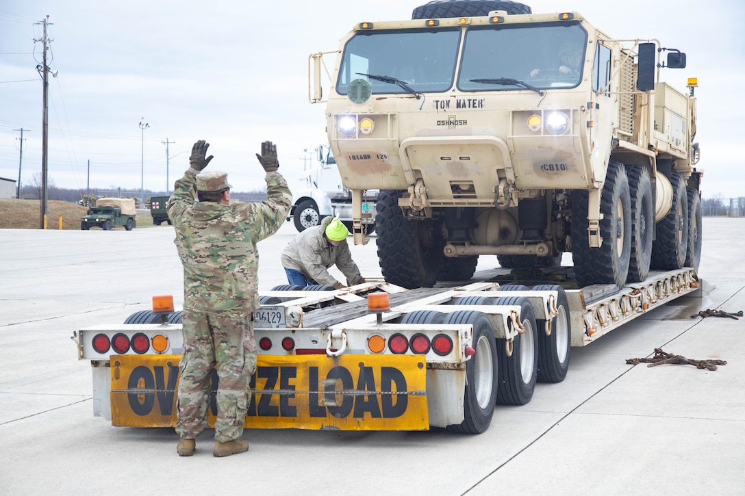 A soldier guides a military vehicle onto a commercial line haul truck.