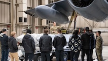 A member of the 5th Maintenance Group presents atop a munition loading trailer to Minot State University Track & Field Team students at Minot Air Force Base, North Dakota, March 4, 2025. Many of the students had prior knowledge of the Air Force’s presence but were not educated on the greater mission of the base. (U.S. Air Force photo by Senior Airman Kendra A. Ransum)